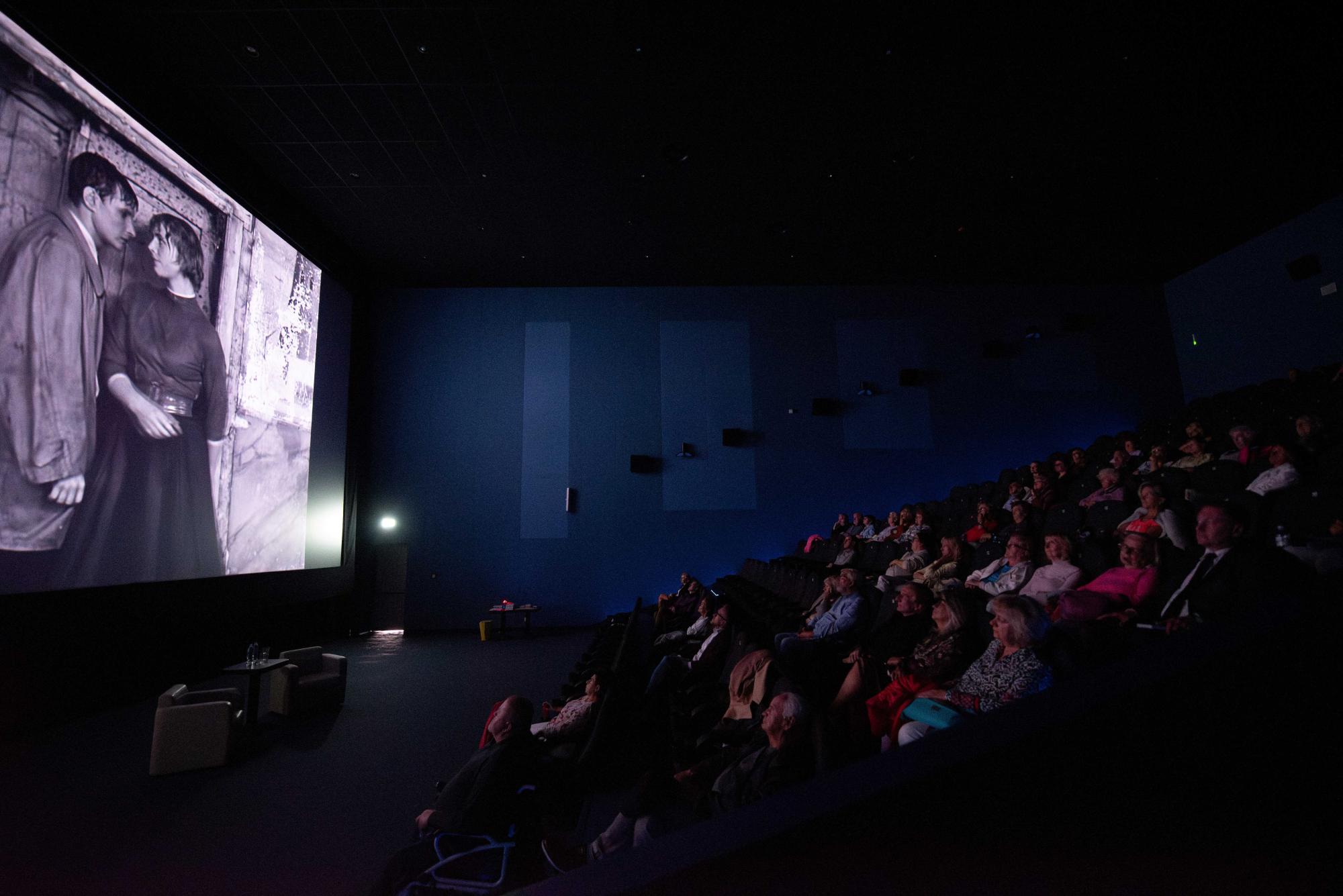 Na dużym ekranie wyświetlany jest film o Wojciechu Kilarze, publiczność siedzi w rzędach w sali kinowej