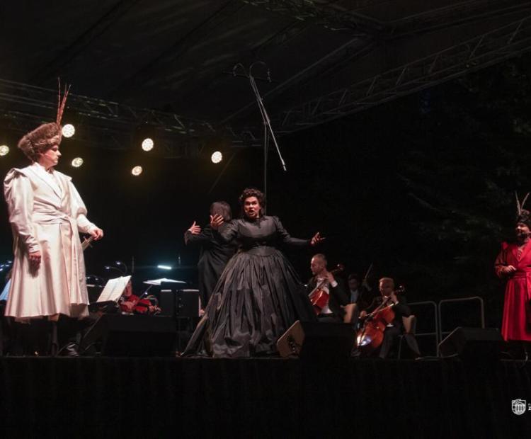 Soliści Polskiej Opery Królewskiej stoją na estradzie w strojach historycznych - białym surducie i czarnej sukni - i wykonują operę Straszny dwór Stanisława Moniuszki