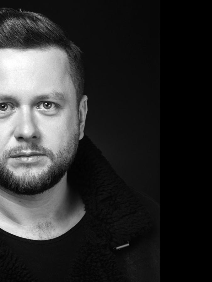 Kompozytor i pianista Paweł Tomaszewski pozuje do zdjęcia z czarnej skórzanej kurtce, twórca ma krótki zarost i ciemne włosy
